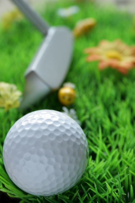 Golfball and club on artificial grass, Golfball in the foreground, out-of-focus golfclub and plastic yellow bee in the background on artificial grass, light from top, fill light in the front