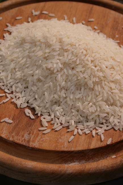A pile of rice corns on a wood board, A pile of rice corns on a brown board of wood. crisp focus in the foreground and a bit of bukeh in the background. Light from top right.
