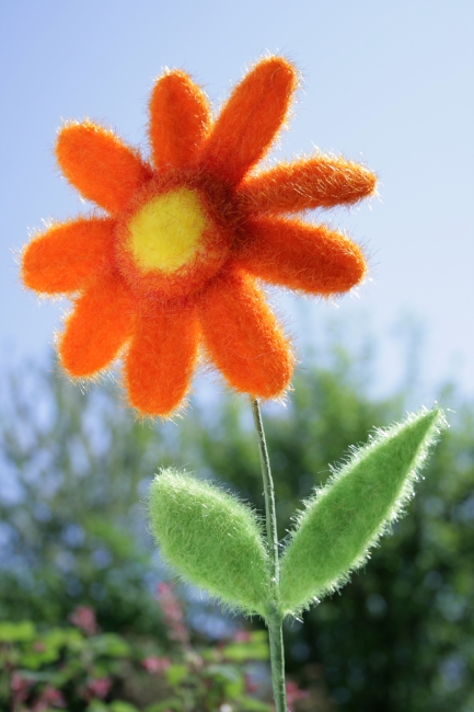 Artificial orange flower, An artificial orange flower with green leafes against a blurry background of sky and green