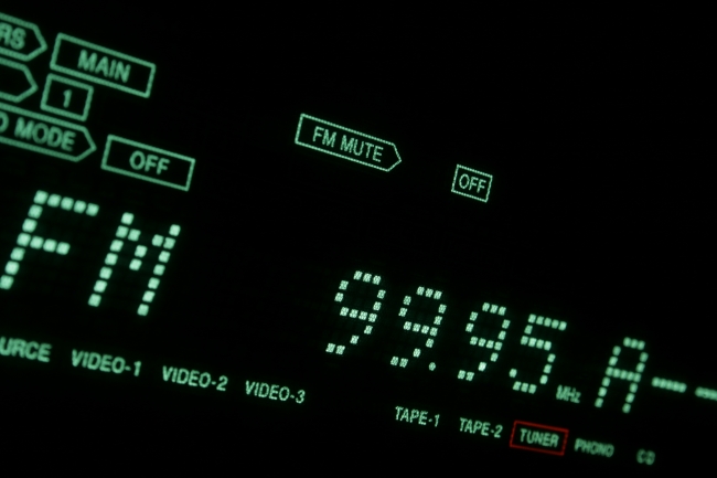 Green Hi-Fi LCD display in close-up TUNER/FM, A hi-fi receiver's green dot-matrix LCD display in extreme close-up showing FM 99.95 (tuner). Tilted view with green font on black background.