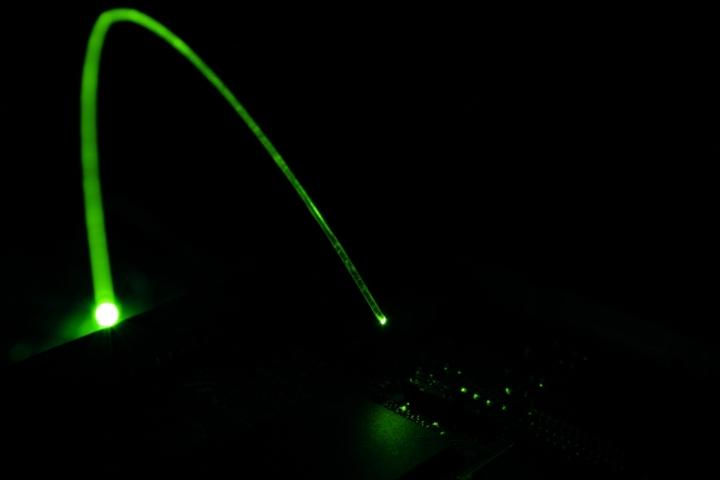 Fiber optic green illuminating part of a circuit board, A green glowing fiber optic cable emitts light on a part of a circuit board revealing integrated-circuits