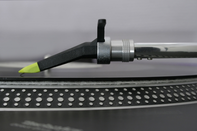DJ turntable needle in close-up, sideview, Close-up sideview of a deejay turntable's pick-up system, a Concorde style Ortofon Night Club needle with yellow tip placed on the rim of the record, speed m...