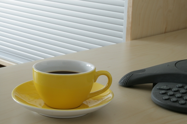 Yellow cup filled with coffee on a table next to a Polycom conference phone, 