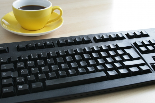 Cup of coffee on a table next to a black Cherry keyboard, 