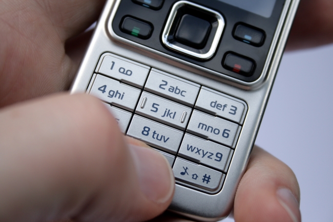 Cell phone keypad in palm, A hand holding a modern silver Nokia 6300 cellular mobile phone, the thumb pressing the zero key