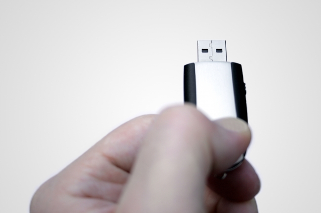 USB stick with hand, A hand holding a silver-black USB stick as if the person whould insert it into the computer, against a white gradient background