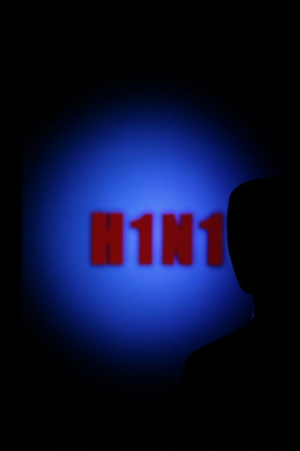 Looking towards H1N1, A man is looking into a room where on blue background H1N1, the abbreviation of the swine flu influenza virus, is written in red glowing letters.