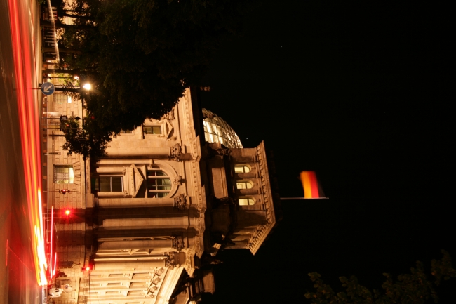 At the corner of the German Reichstag, the German flag waving over a busy street at night, long exposure rendering taillights as streams of light